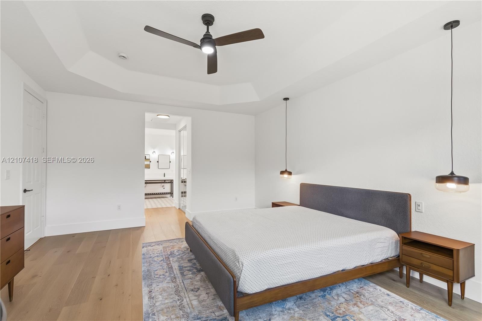Tray ceiling, wood-finish flooring, matte black ceiling fan, and dual suspended pendant light fixtures
