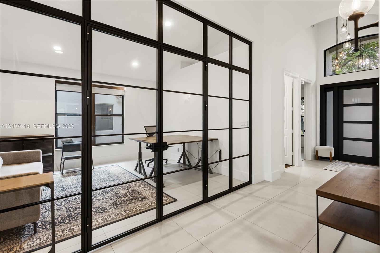 Floor-to-ceiling iron-frame glass room divider, recessed lighting, tile flooring, arched entryway, and front door with glass inserts