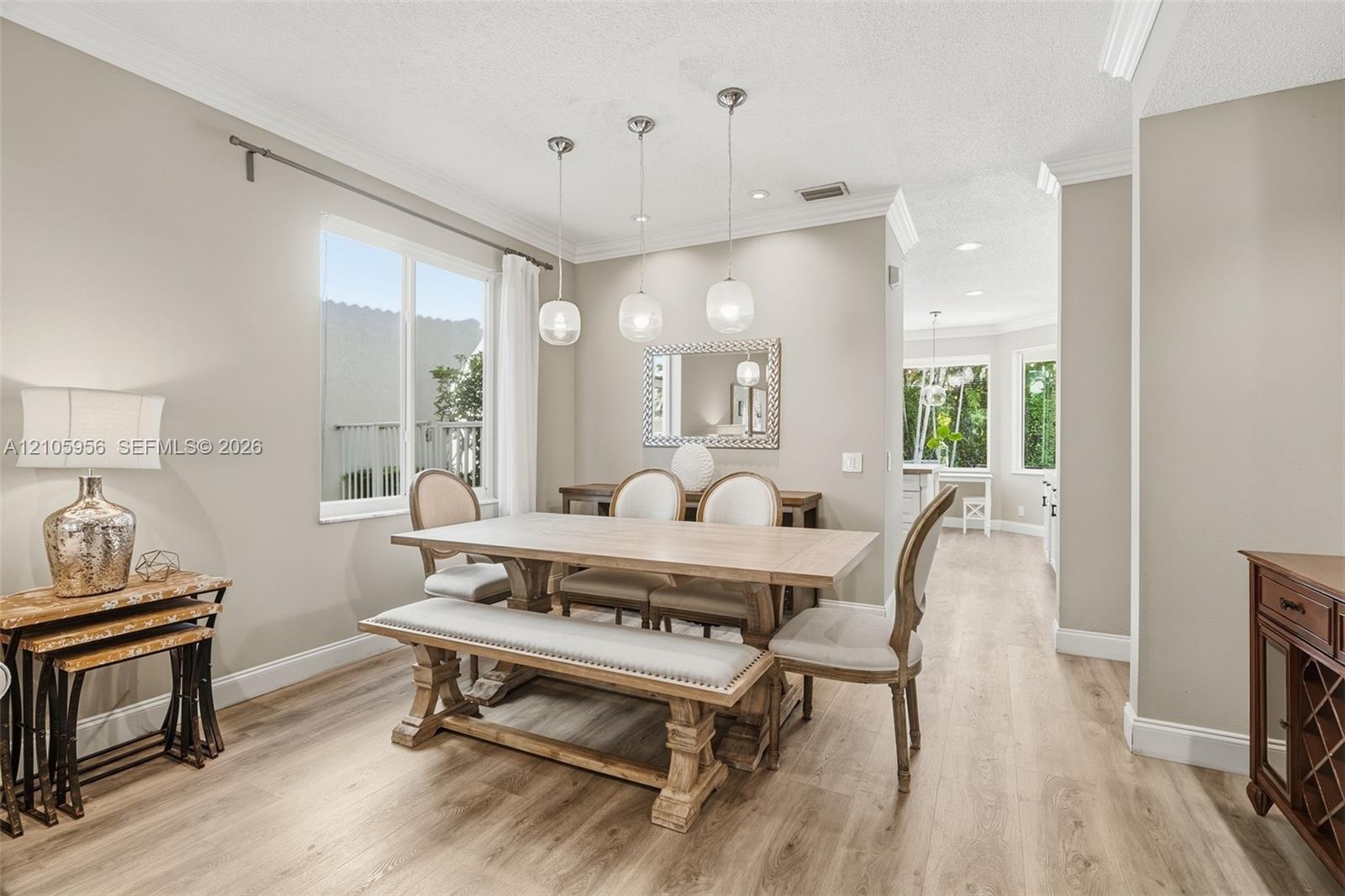 Dining area featuring wood-finish flooring, crown molding, and three globe pendant light fixtures