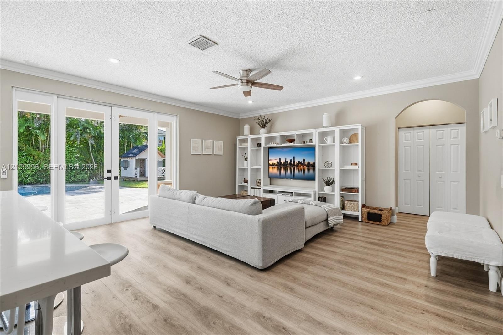 Living area featuring wood-finish flooring, crown molding, recessed lighting, built-in floor-to-ceiling shelving, and multi-panel glass patio doors