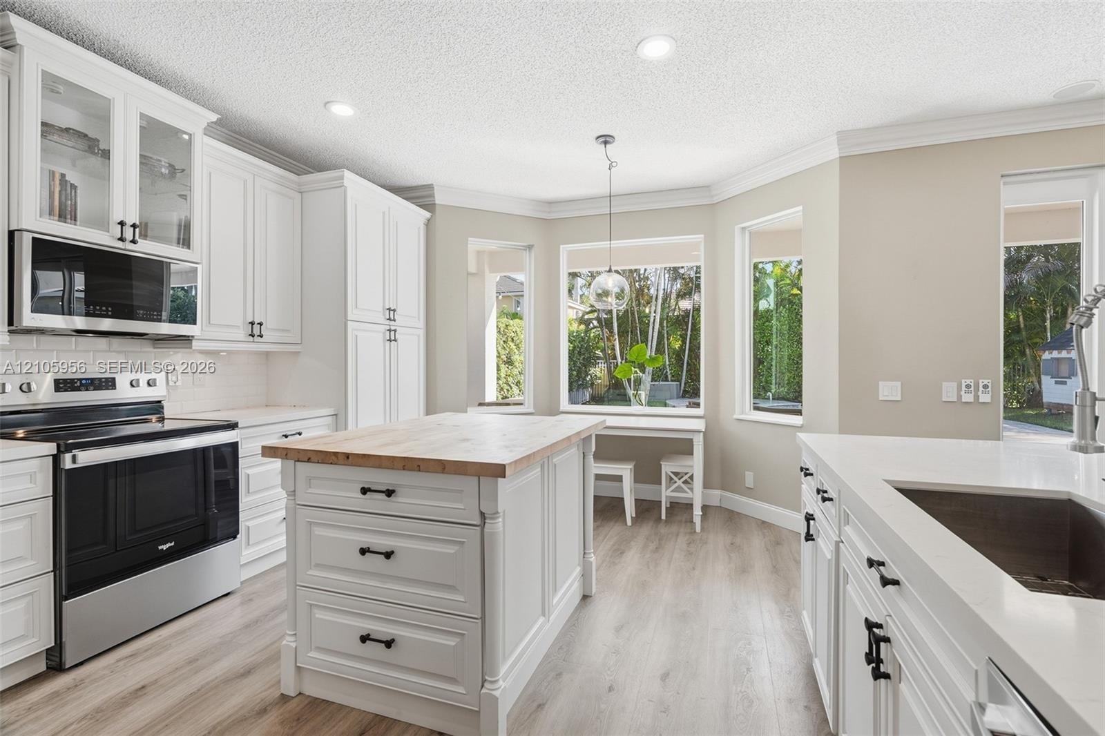 Kitchen featuring white shaker-style cabinetry, wood-top center island, stone-surfaced countertops, stainless steel appliances, and wood-finish floori