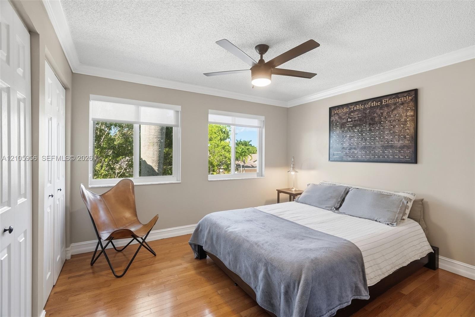 Room featuring wood-finish flooring, dual windows with roller shades, ceiling fan with integrated lighting, and multi-panel closet doors