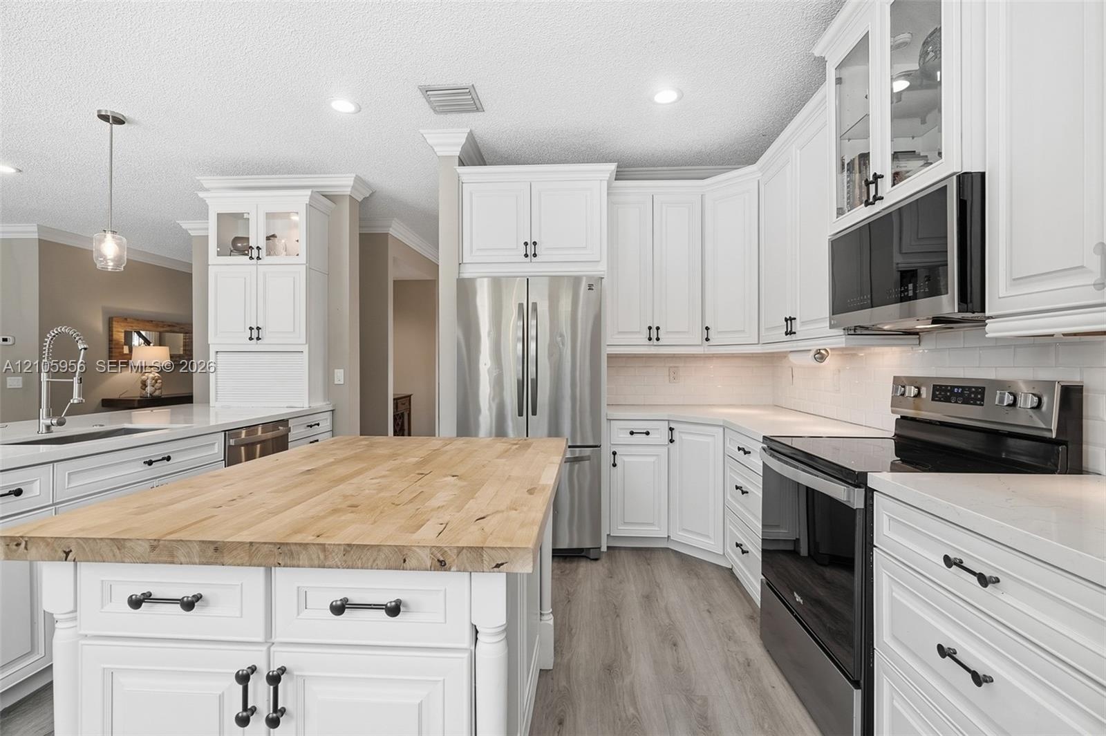 Kitchen featuring white shaker-style cabinetry, wood-top center island, stainless steel appliances, light-toned countertop surfaces, and wood-finish f