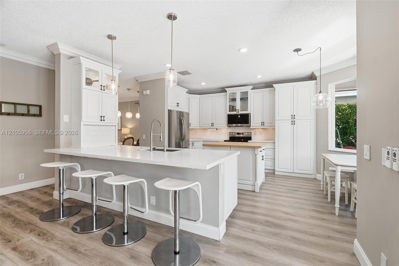 Kitchen featuring white shaker-style cabinetry, quartz countertops, a central island with a wood-finish surface, wood-finish flooring, and recessed pe