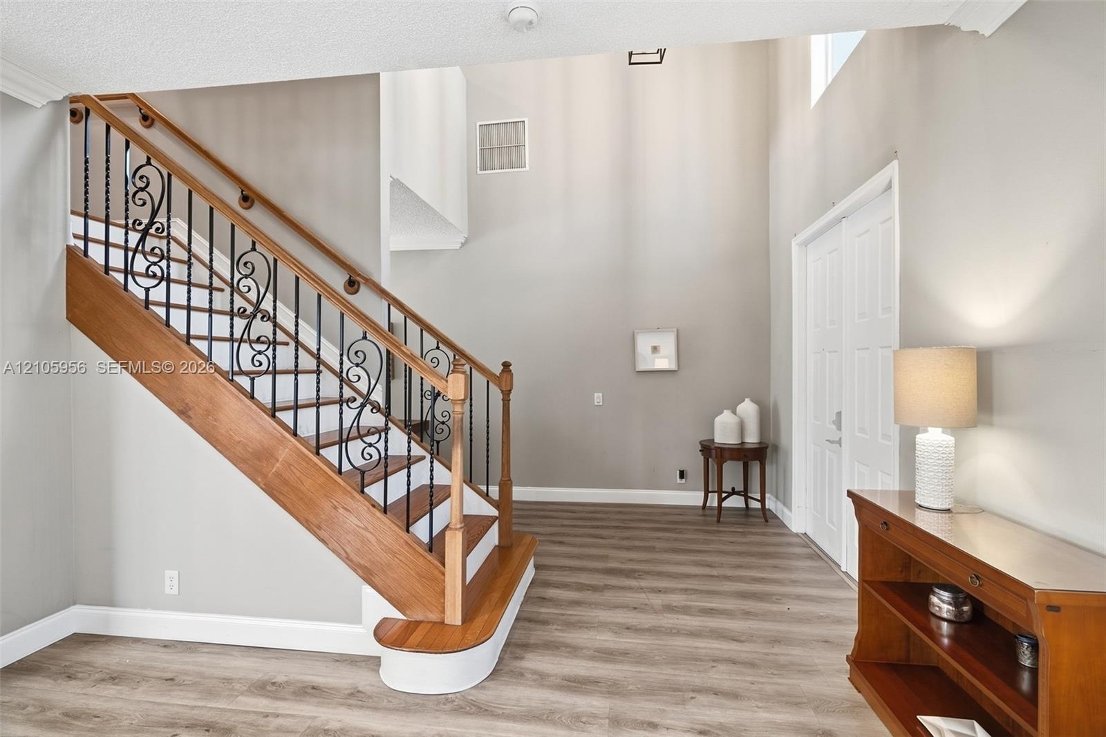 Two-story foyer featuring high ceilings, wood-finish flooring, and a staircase with decorative wrought-iron balusters and a natural wood handrail