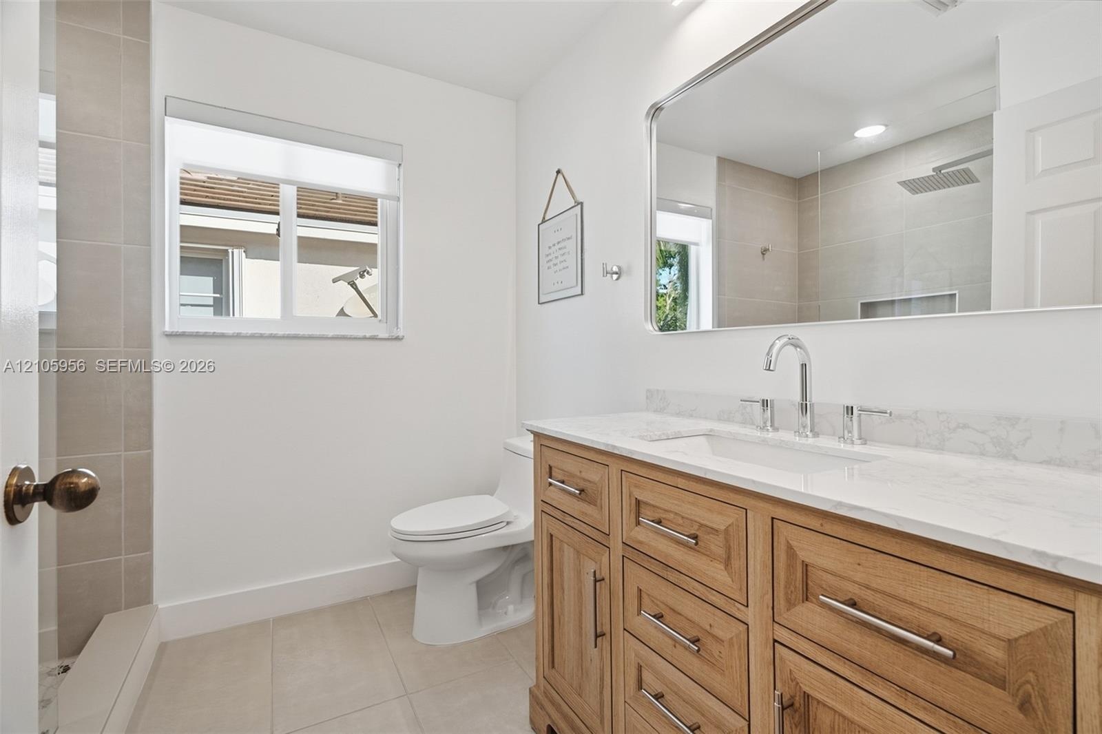 Bathroom featuring a natural wood-finish vanity with stone-look countertop, rectangular undermount sink, large wall-mounted mirror, and tile-surround 