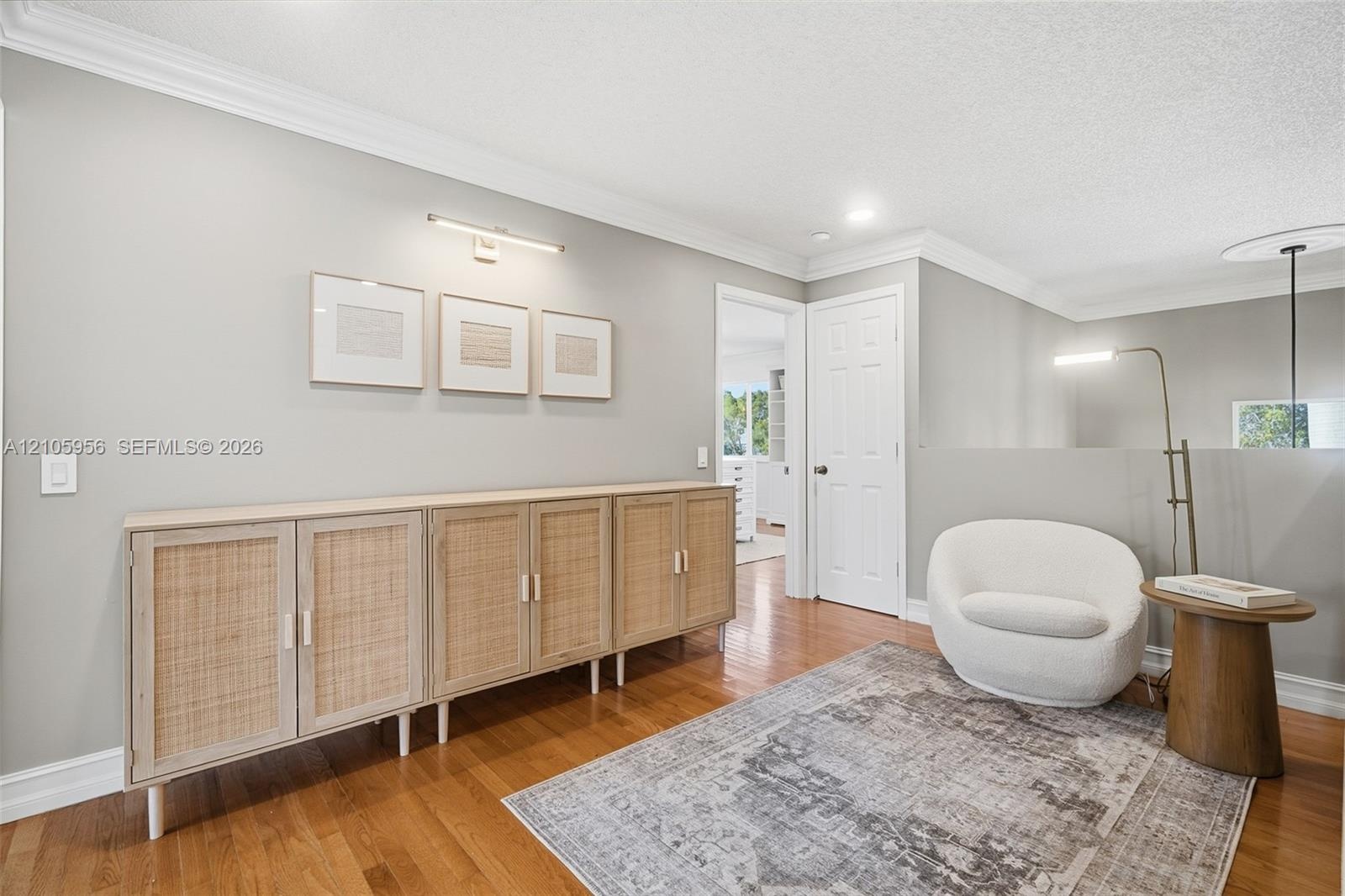 Interior space featuring wood-finish flooring, crown molding, a built-in multi-door cabinetry unit, and a wall-mounted picture light