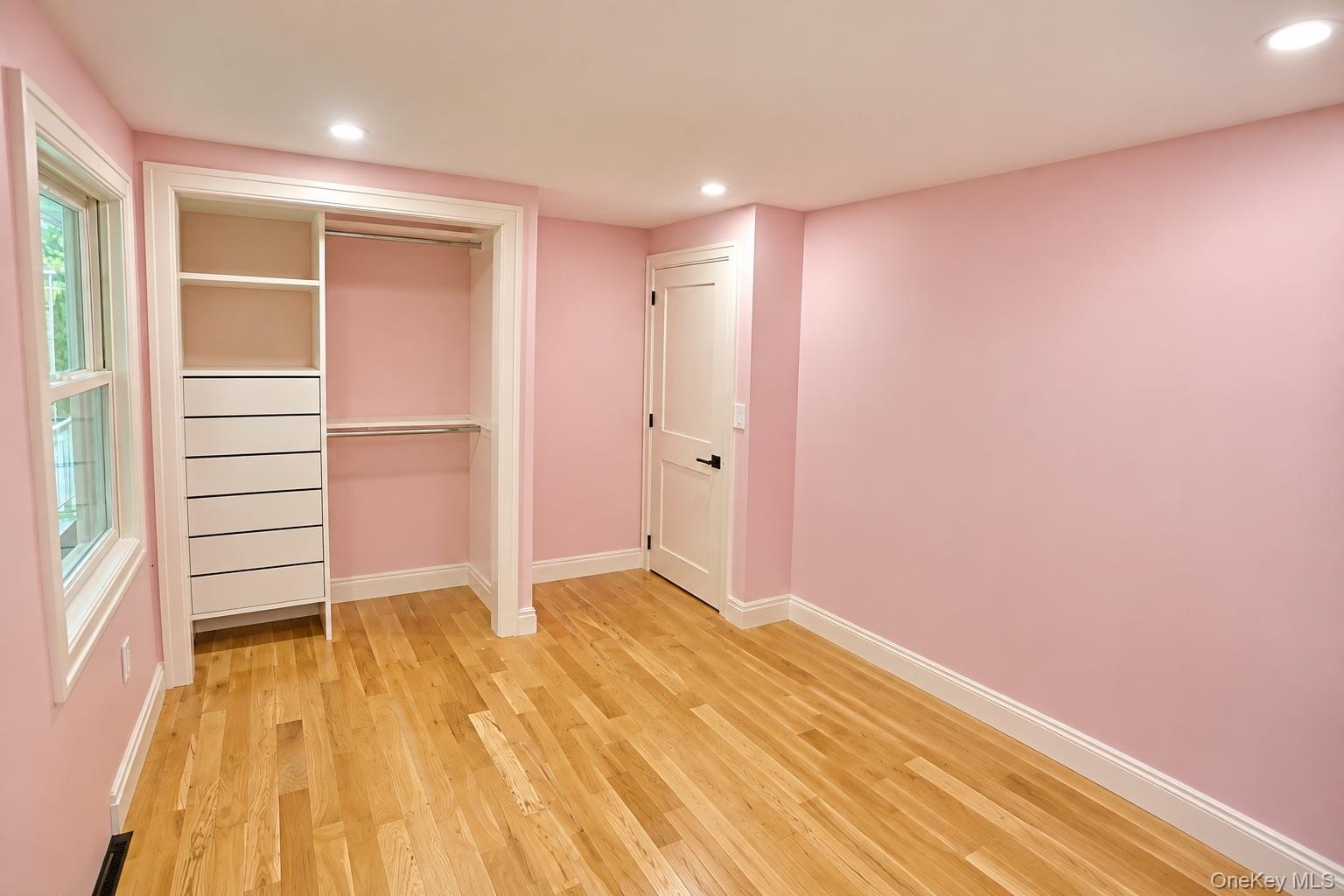 Interior space featuring wood-finish flooring, built-in closet organization with integrated drawer storage, a two-panel interior door with matte black