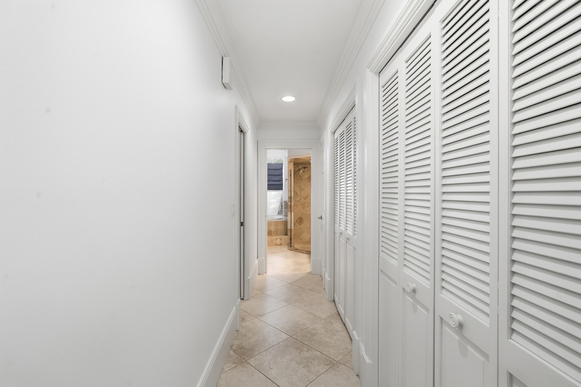 Hallway featuring recessed ceiling lighting, tile flooring, and custom louvered closet doors with polished hardware