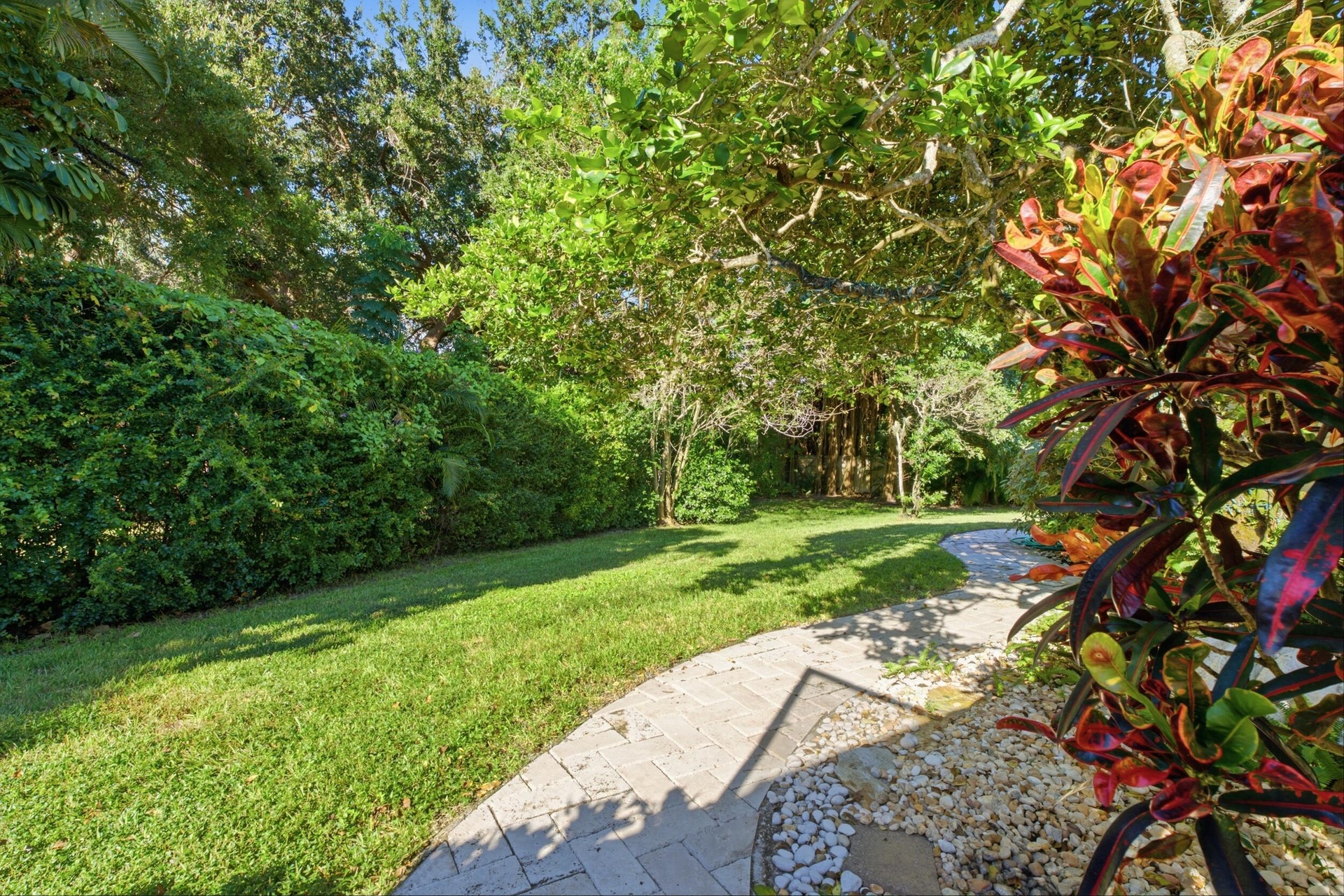 Expansive backyard featuring a brick paver walkway, manicured lawn, established landscaping, and mature trees