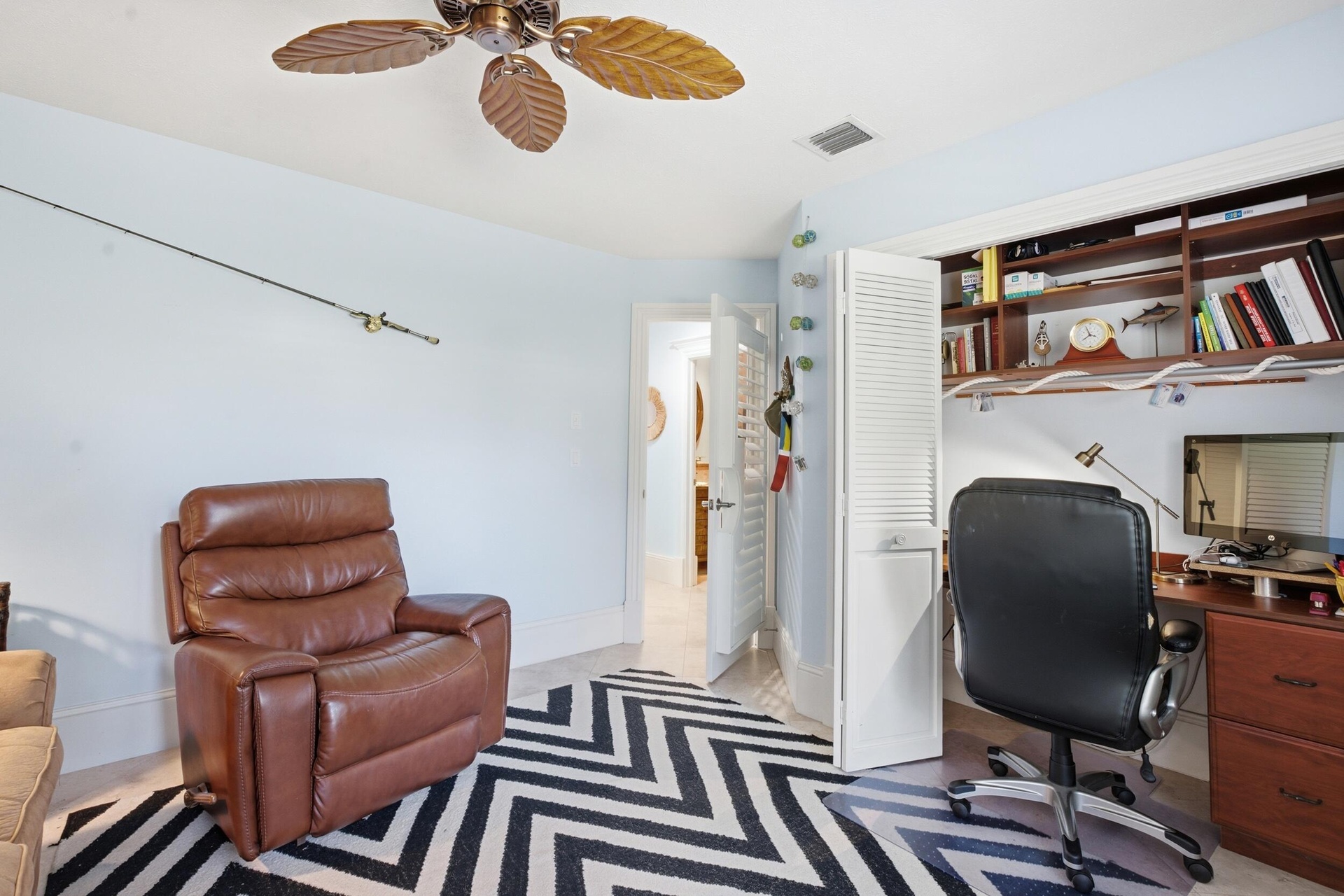 Room featuring a built-in wooden desk with overhead shelving, louvered closet doors, and an attached palm-leaf style ceiling fan