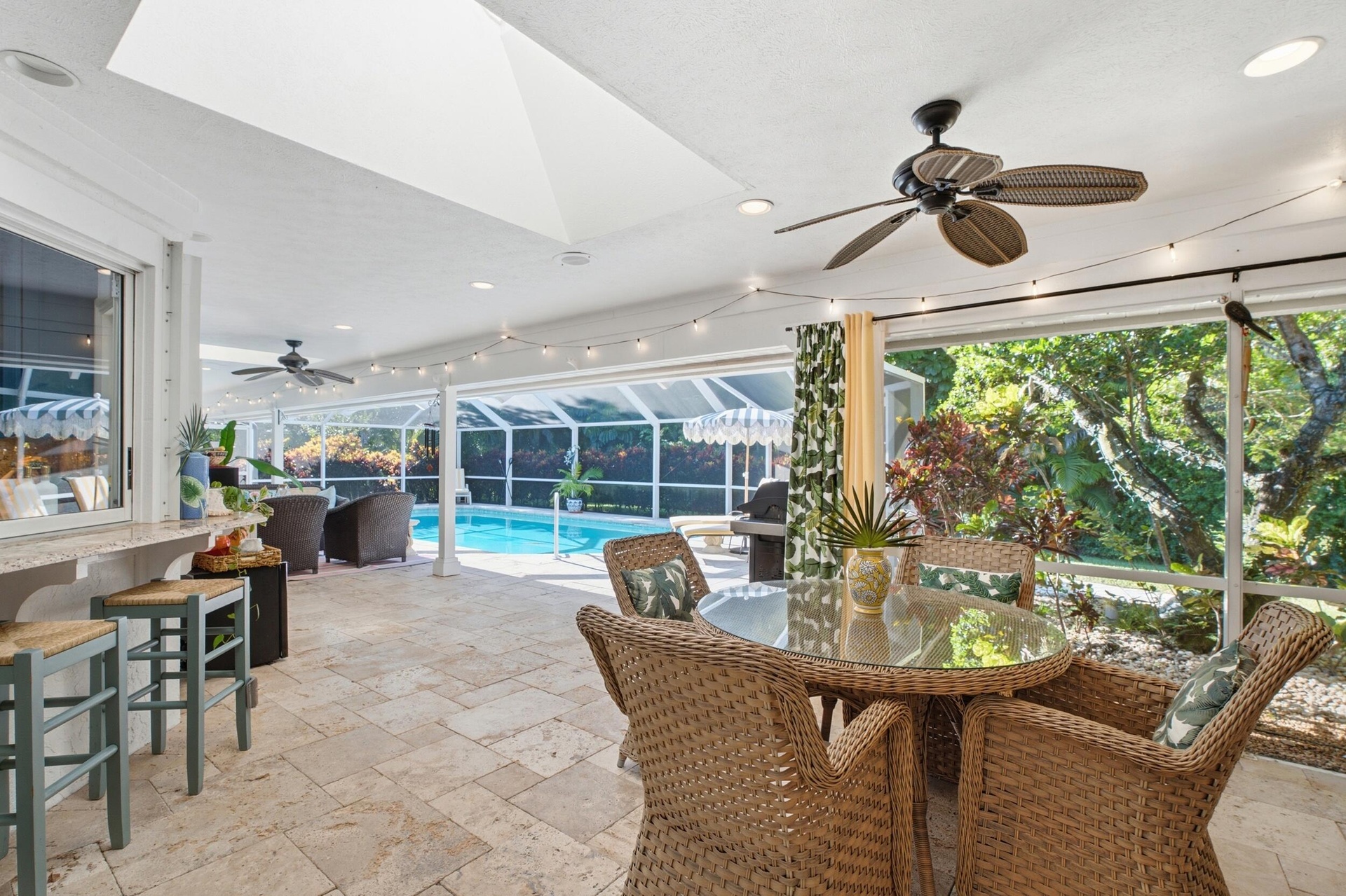 Screened-in lanai featuring stone tile flooring, a built-in stone countertop pass-through, a vaulted ceiling with skylights, multiple ceiling fans, an