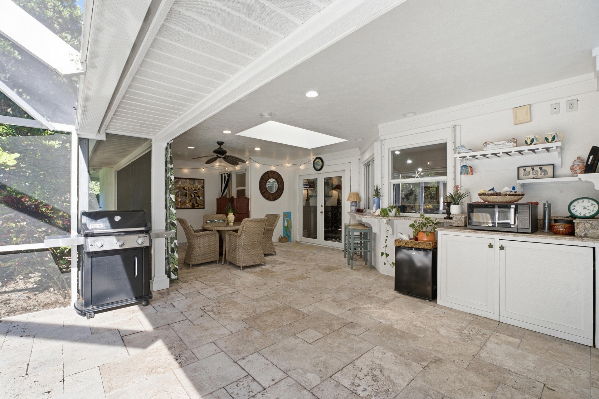 Screened outdoor living area featuring stone-tile flooring, a vaulted ceiling with a skylight, recessed lighting, and built-in cabinetry with stone co