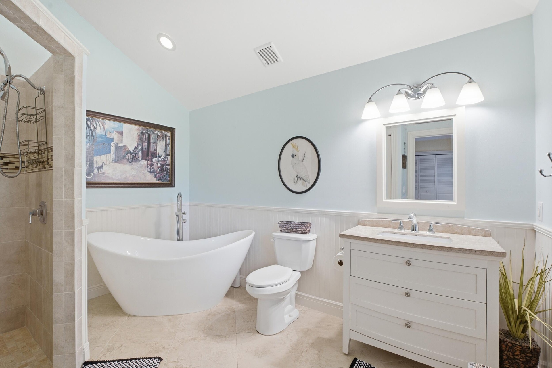 Bathroom featuring a freestanding soaking tub, a vanity with a light-toned countertop and integrated sink, a walk-in tiled shower, white beadboard wai