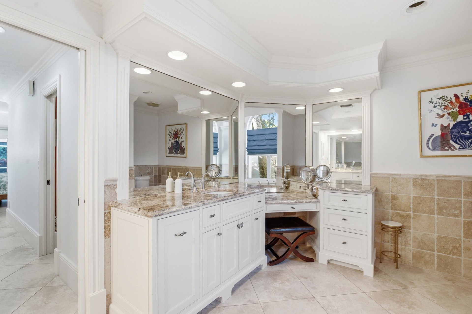Custom white cabinetry with multi-drawer storage, integrated vanity station, stone-surfaced countertop, large vanity mirrors, and wall-tile wainscotin