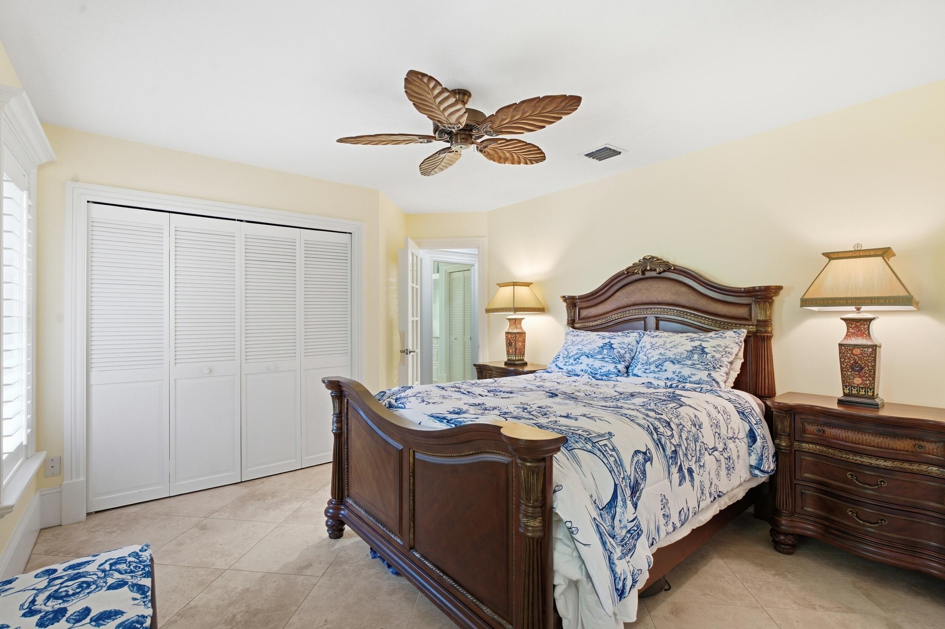 Neutral tile flooring, white louvered closet doors, and palm-leaf style ceiling fan