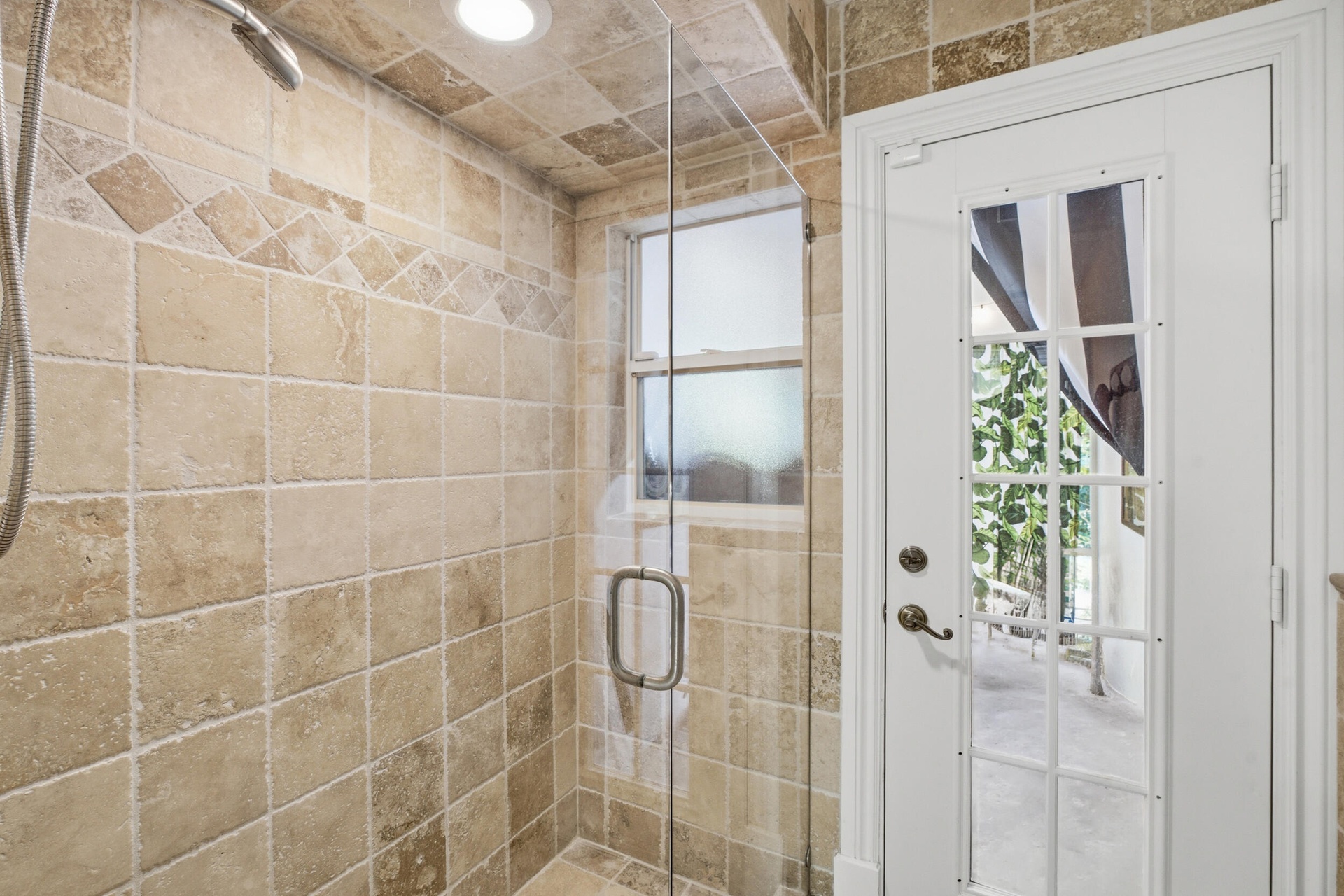 Walk-in shower featuring textured stone tile surround with decorative diagonal inlay, frameless glass enclosure, and an attached glass-paneled exterio