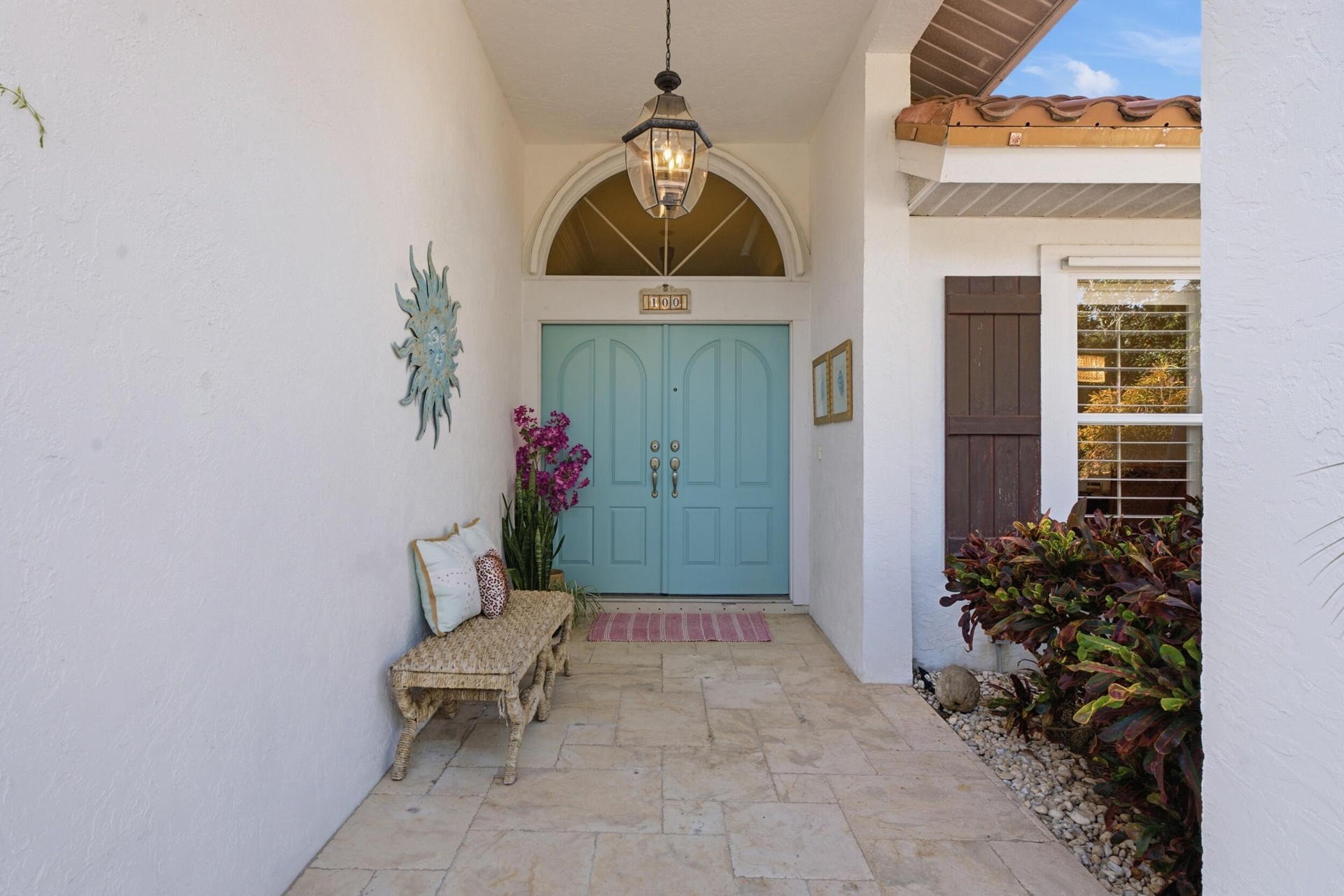 Covered entryway featuring stone-finish flooring, a double-door entry, a prominent arched transom window, a decorative hanging pendant light, and dark