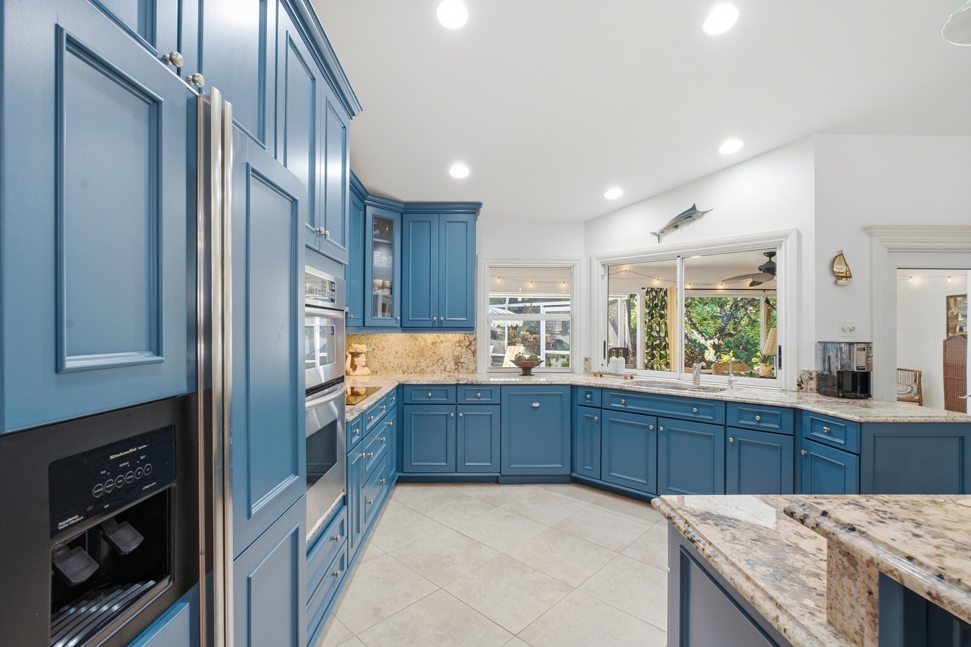 Kitchen featuring custom blue shaker-style cabinetry, natural stone countertops, tile flooring, built-in double wall ovens, and recessed lighting