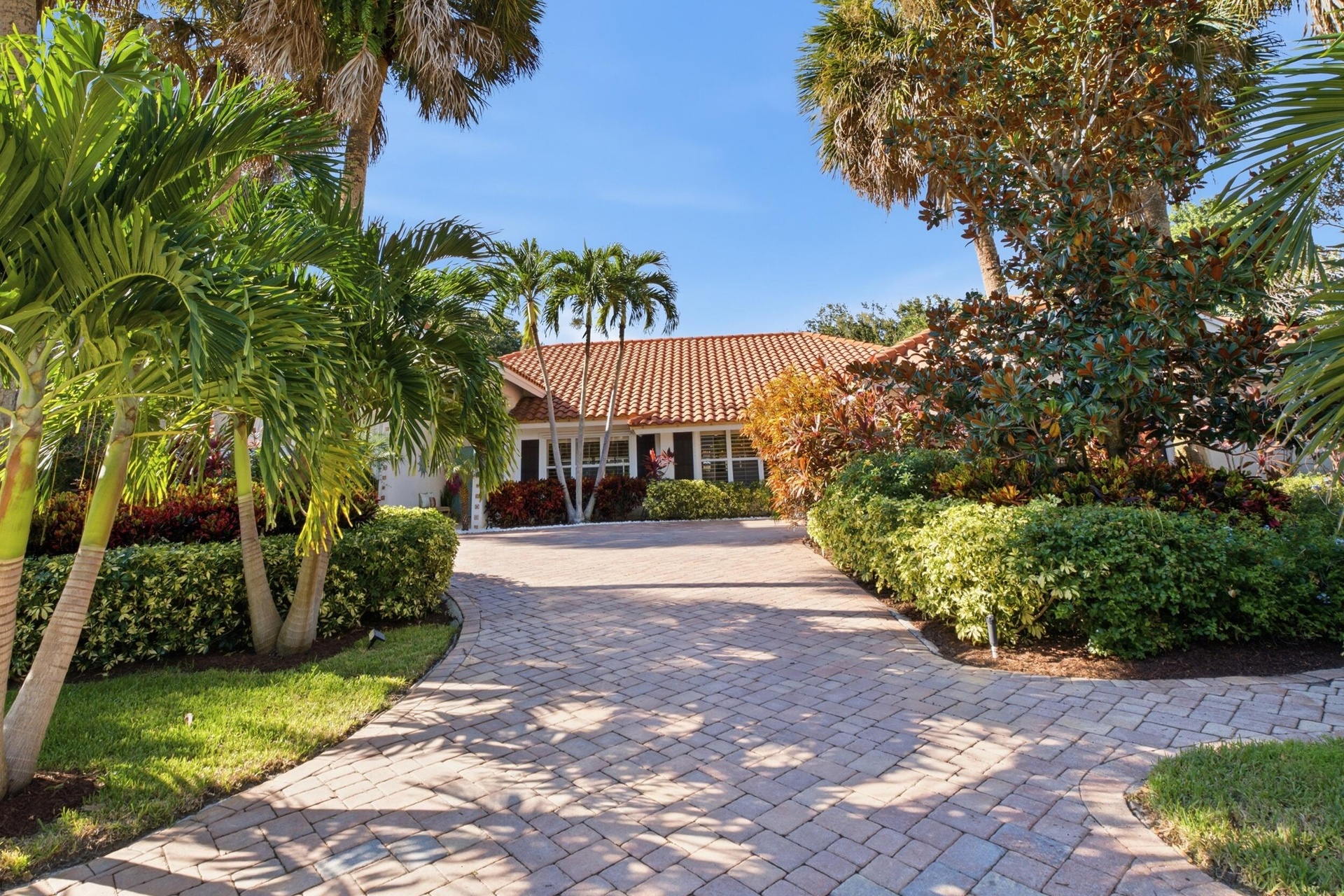 Exterior facade featuring a Spanish-style tiled roof, paver driveway, and mature tropical landscaping