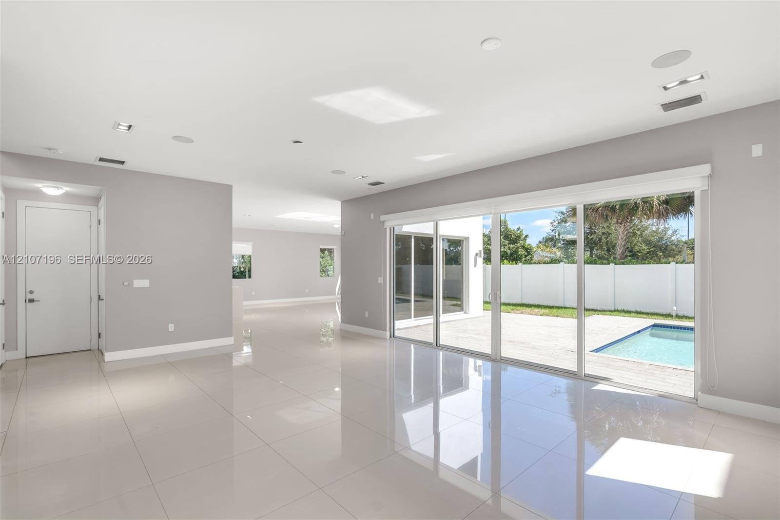 Large format tile flooring, recessed lighting, ceiling-mounted speakers, and expansive floor-to-ceiling glass sliding doors opening to a concrete pati