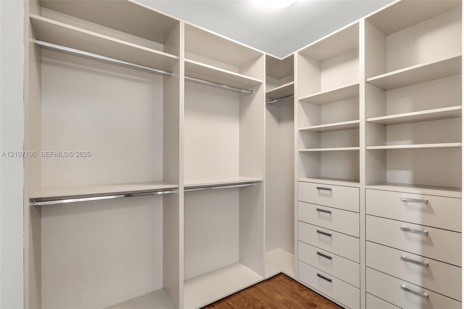 Custom walk-in storage featuring floor-to-ceiling shelving, integrated stainless steel hanging rods, and multiple soft-close drawers with metallic pul