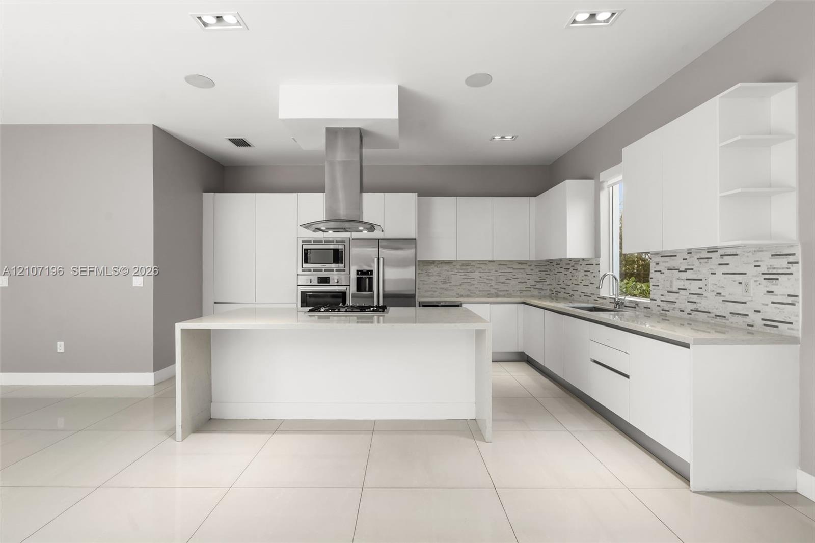 Kitchen featuring flat-panel cabinetry, a central island with a waterfall countertop, stainless steel appliances, a linear-patterned backsplash, and l