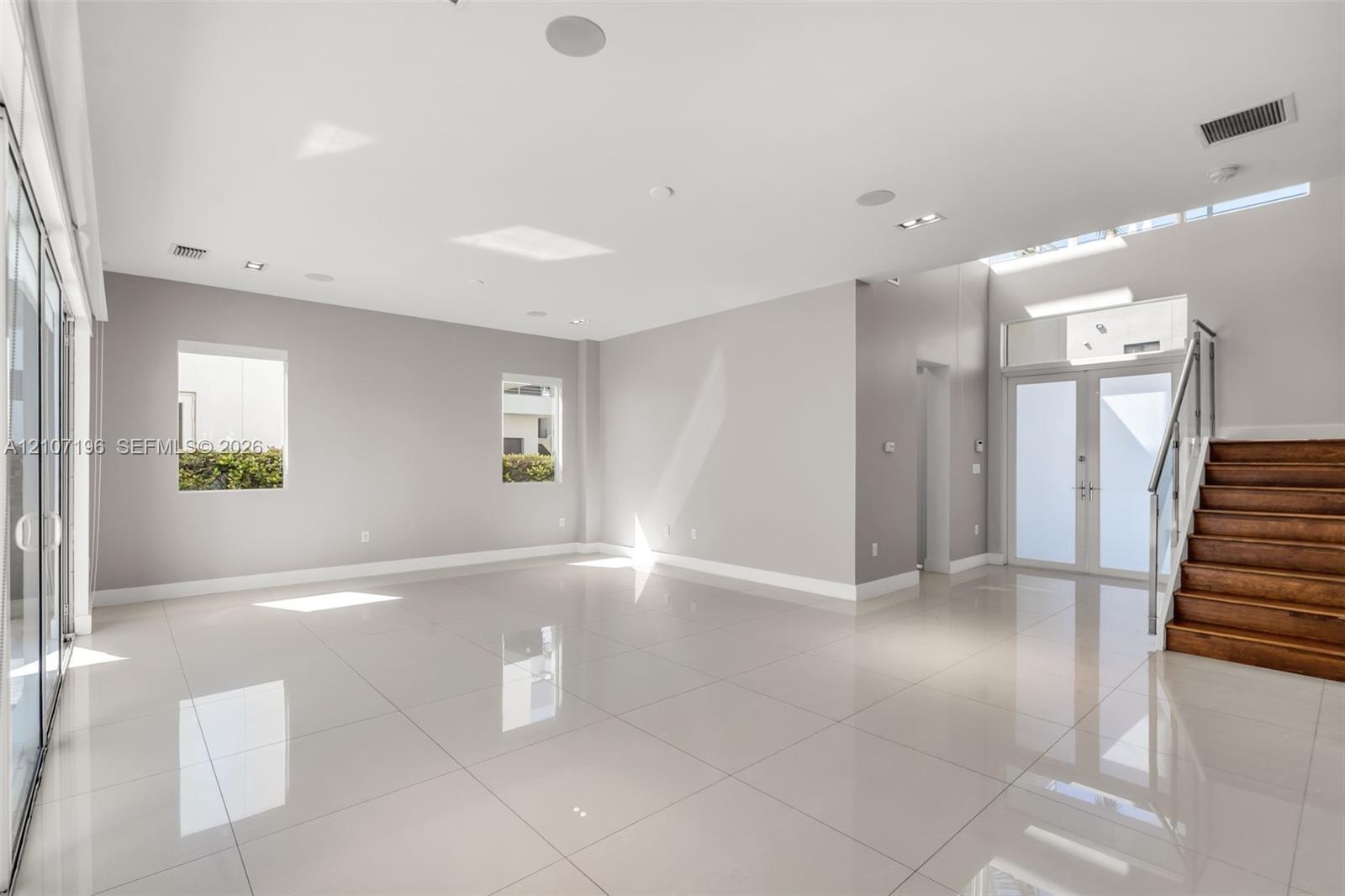 Open-concept interior featuring large-format tile flooring, recessed ceiling lighting, a wood-tread staircase with glass railing, and oversized glass 