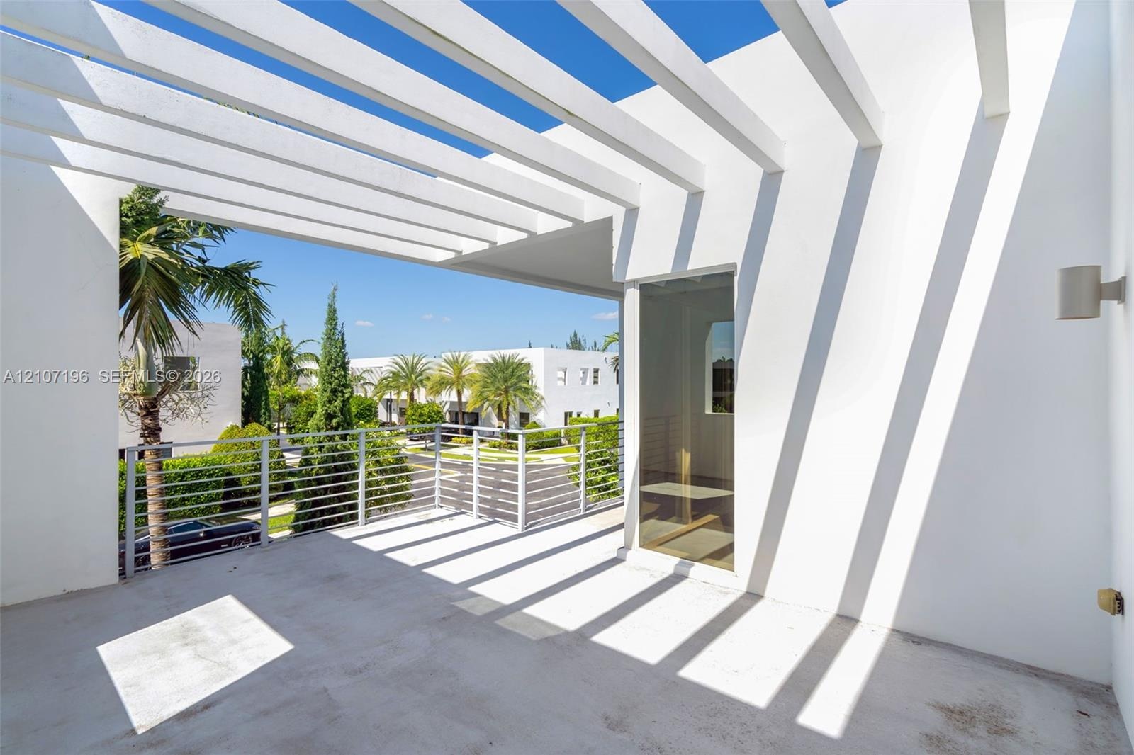 Covered balcony featuring an overhead pergola, concrete flooring, horizontal cable railing, and a wall-mounted cylinder light fixture