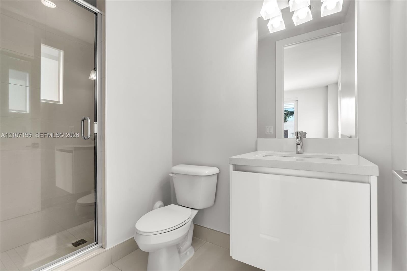 Bathroom featuring a modern floating vanity with a neutral-toned countertop, a glass-enclosed shower with tiled flooring, and a wall-mounted light fix