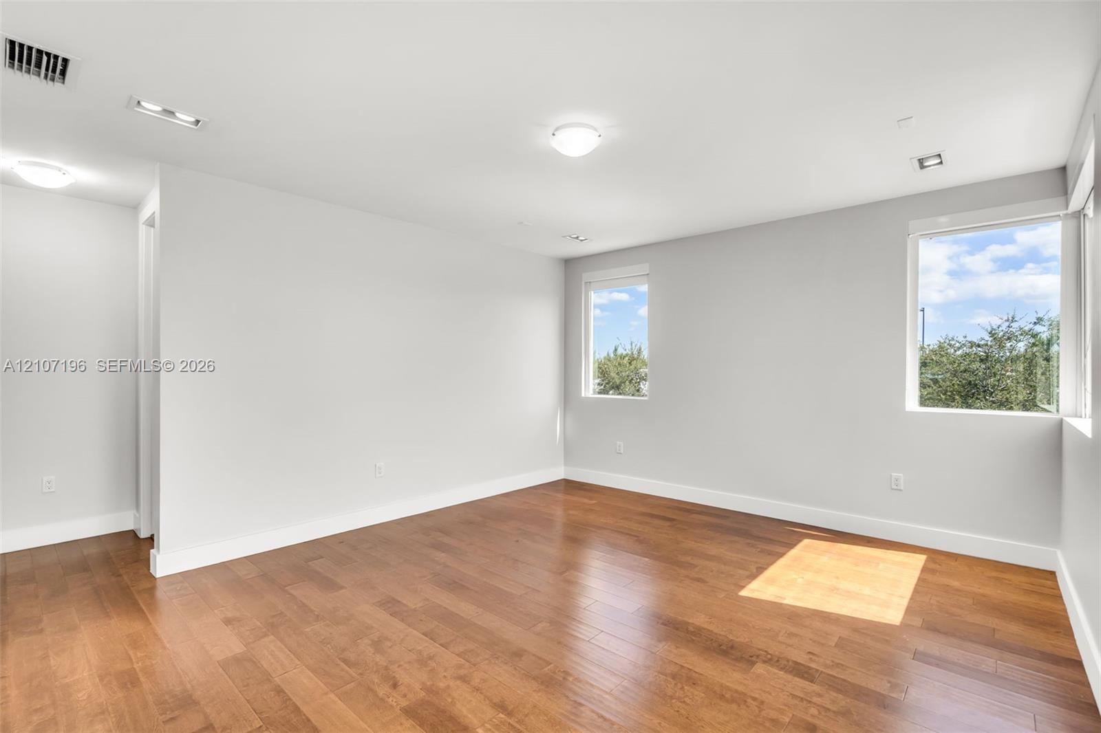 Neutral-toned interior space featuring wood-finish flooring, recessed lighting, and large windows providing natural illumination