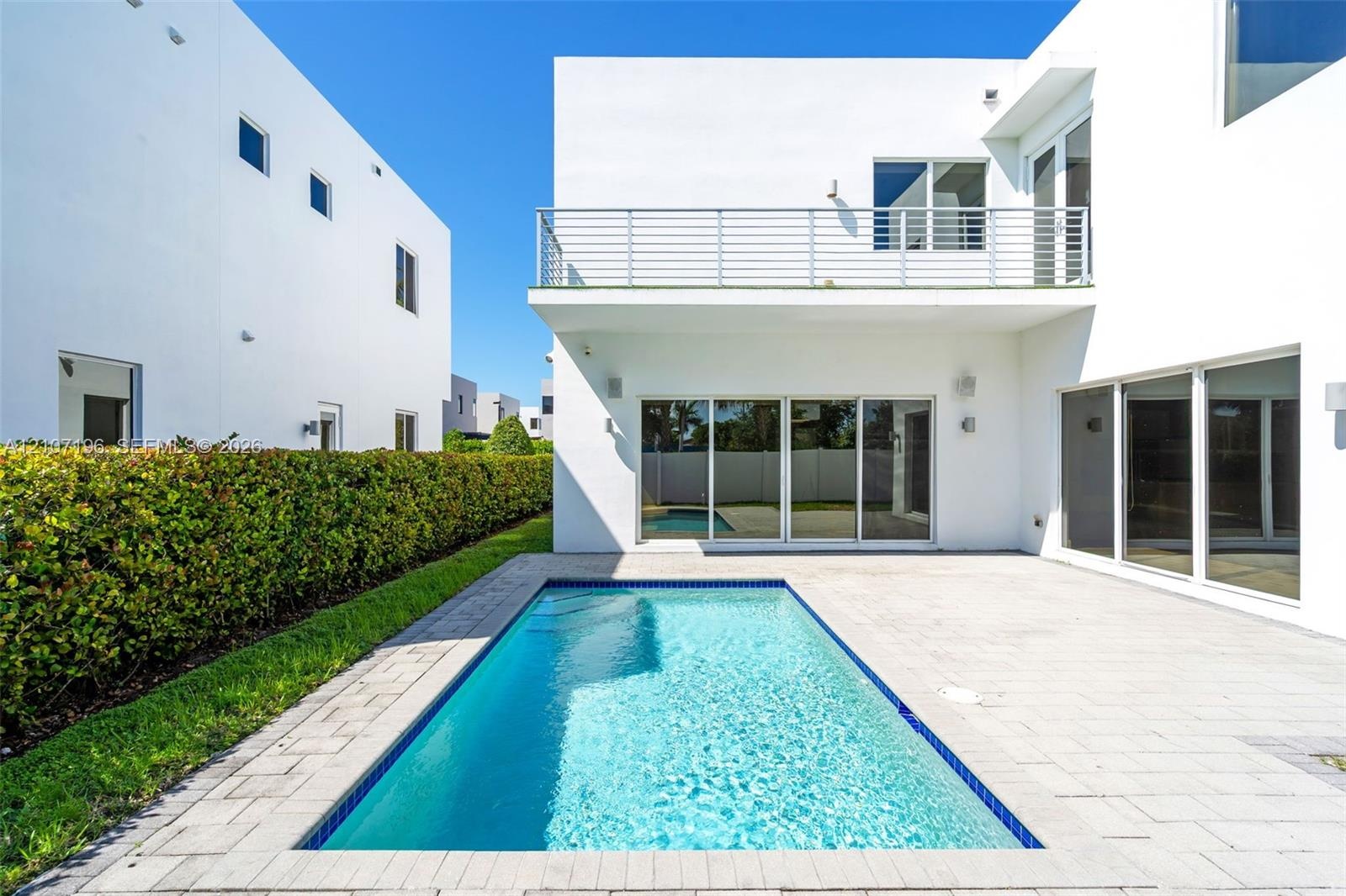 Contemporary exterior featuring a private swimming pool, concrete paver patio, second-story balcony with metal railing, and expansive glass sliding do