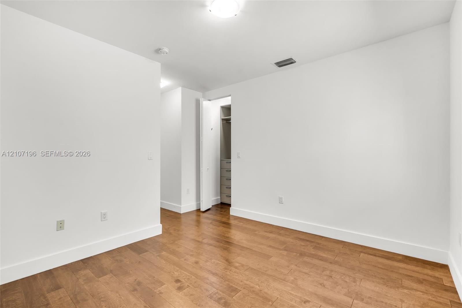 Interior room featuring wood-finish flooring, white walls, and a built-in closet with integrated drawer storage
