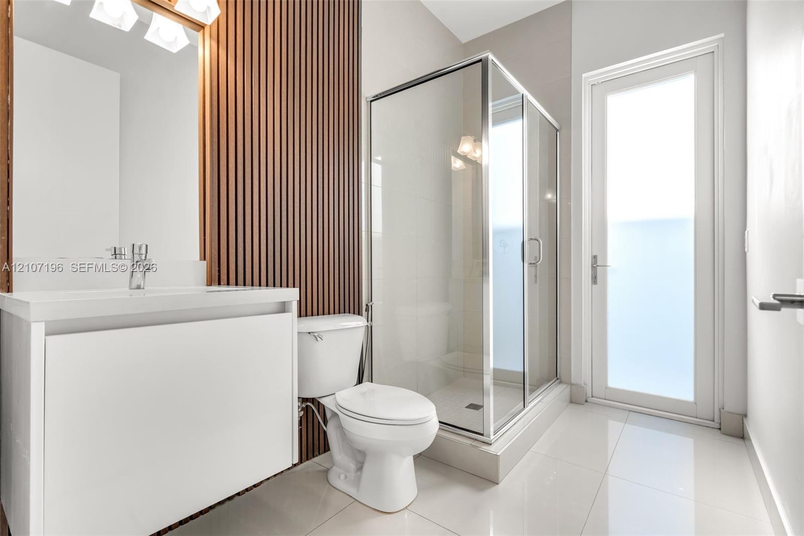Bathroom featuring a white floating vanity, vertical wood-slat accent wall, glass-enclosed shower, polished tile flooring, and a glass-paneled exterio