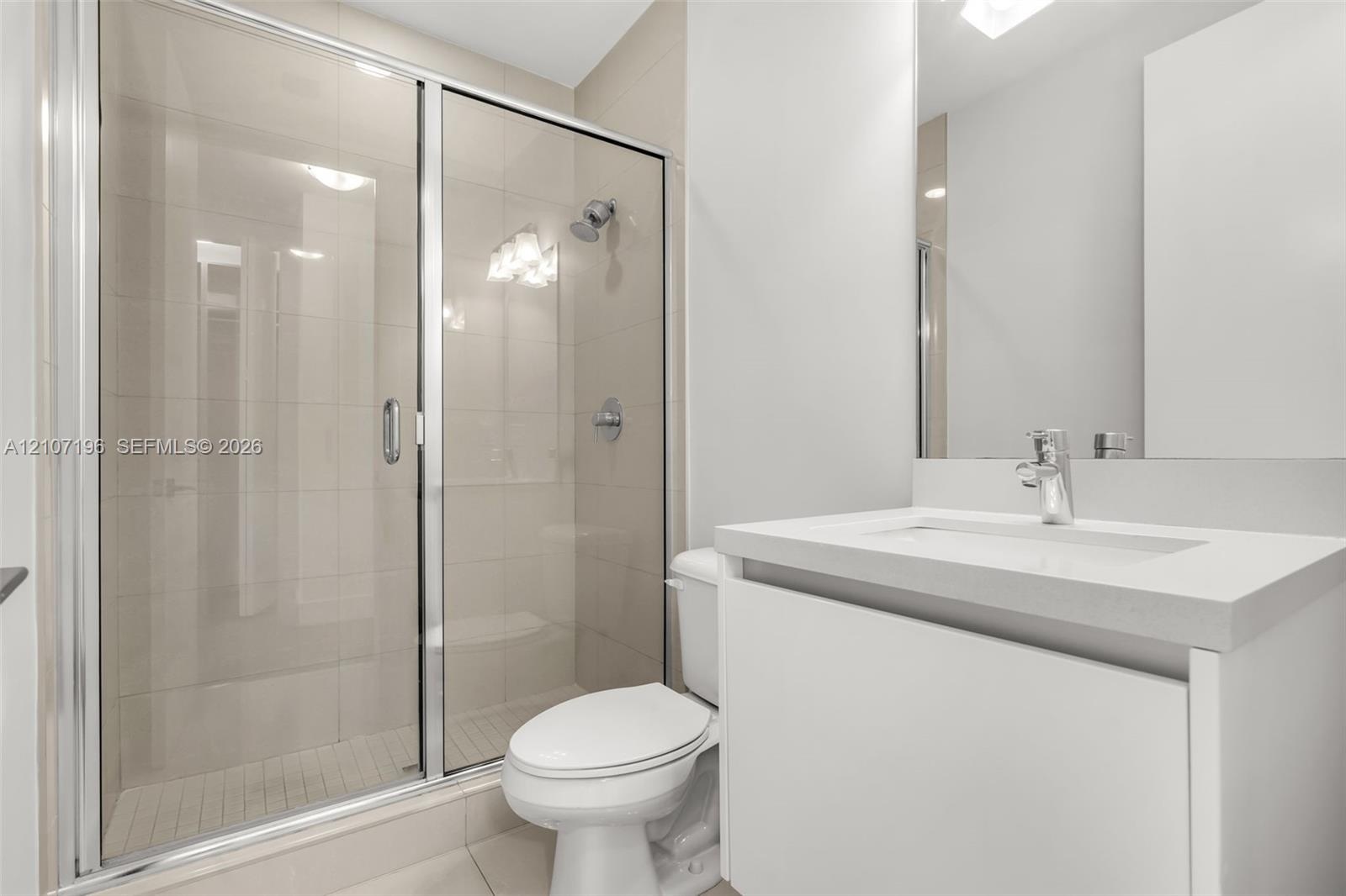 Bathroom featuring a sliding glass shower door, floor-to-ceiling wall tile, white vanity with a solid-surface countertop, and a built-in mirror