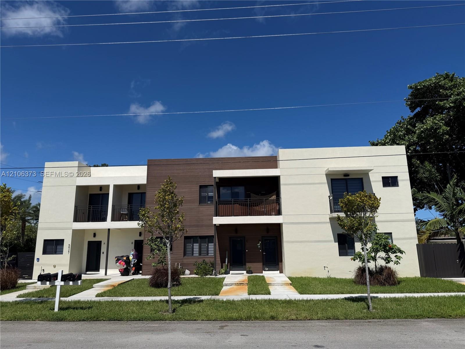 Contemporary two-story exterior featuring multi-textured facade, wood-finish paneling, private balconies with metal railings, and concrete walkways