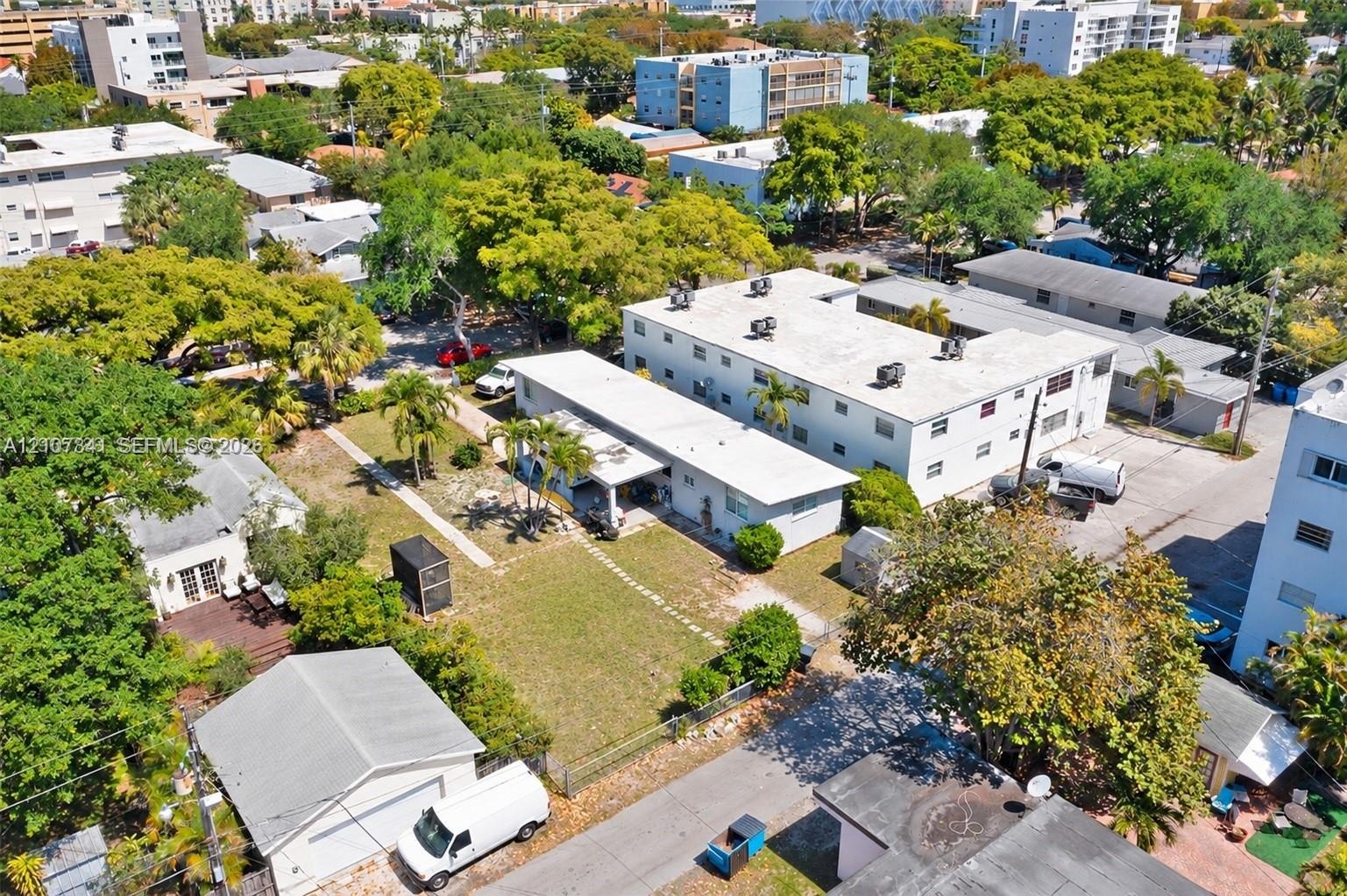 Aerial perspective of a multi-unit residential property featuring a low-rise building, detached garage structure, paved parking area, and mature lands