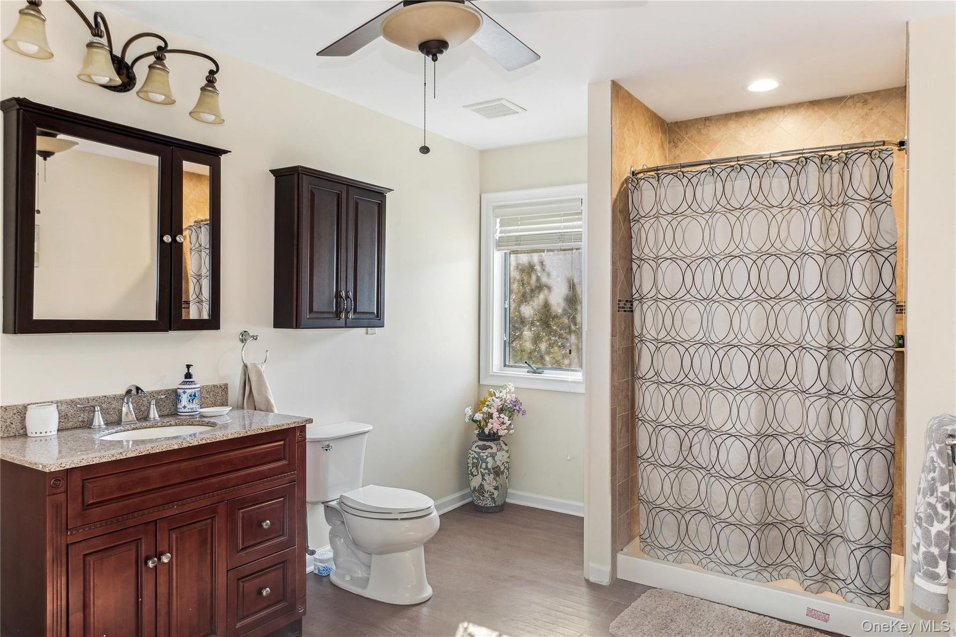 Bathroom featuring hardwood / wood-style floors, curtained shower, vanity, ceiling fan, and toilet