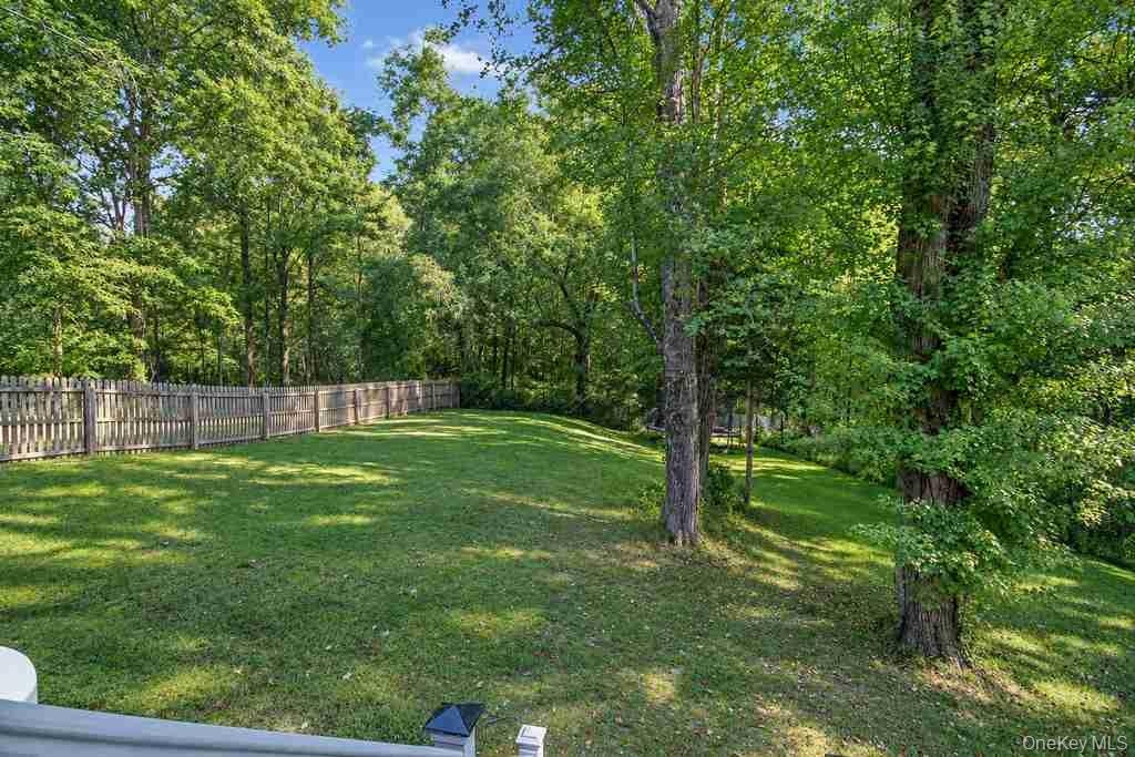 Expansive rear yard featuring a manicured lawn, established picket fencing, and mature trees
