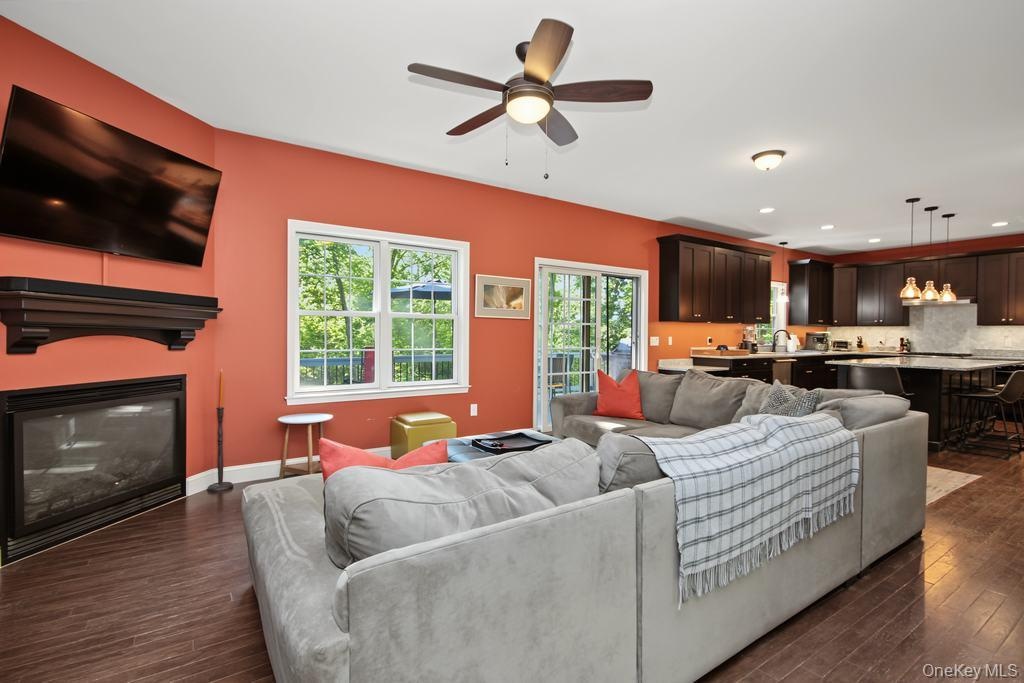 Open-concept living area featuring rich wood-finish flooring, a built-in fireplace with a dark wood mantel, and an integrated kitchen with dark cabine