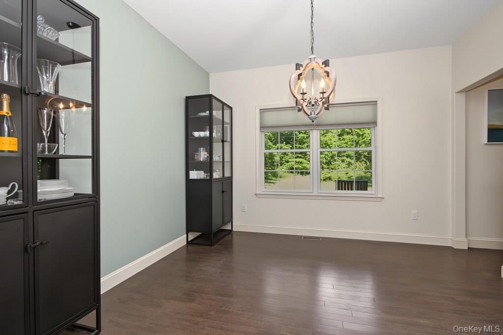 Dining room with vaulted ceiling with a chandelier, wood-finish flooring, and a large window with roller shades