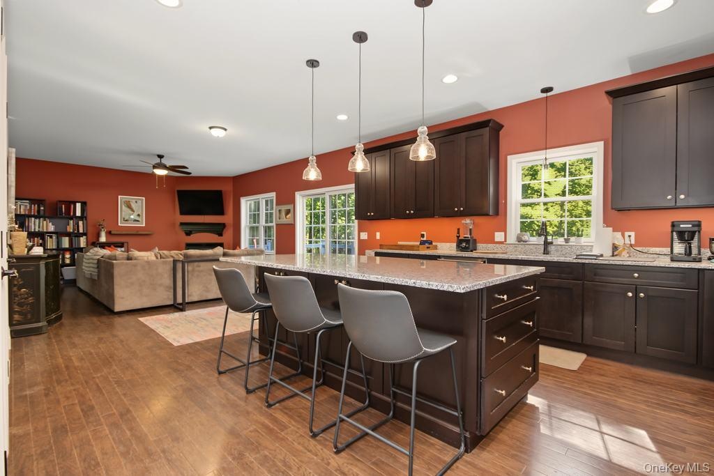 Open-concept kitchen and living area featuring wood-finish flooring, dark wood cabinetry, a center island with a light-toned countertop, and recessed 