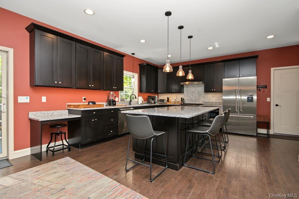 Kitchen featuring dark wood-finish cabinetry, light-toned countertops, a central island with pendant lighting, a stainless steel refrigerator, and woo