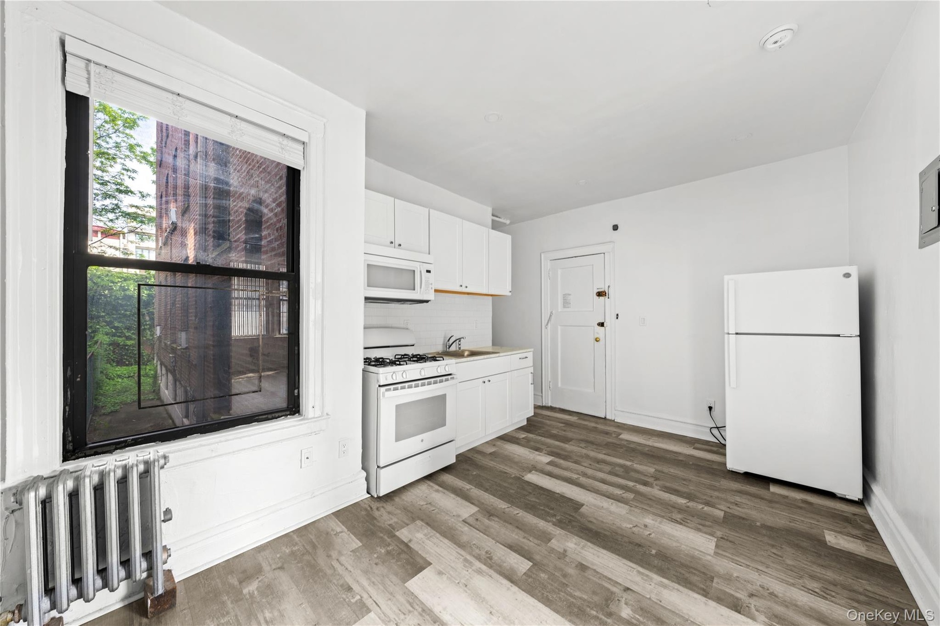 Kitchen with white appliances, radiator, white cabinetry, wood finished floors, and backsplash