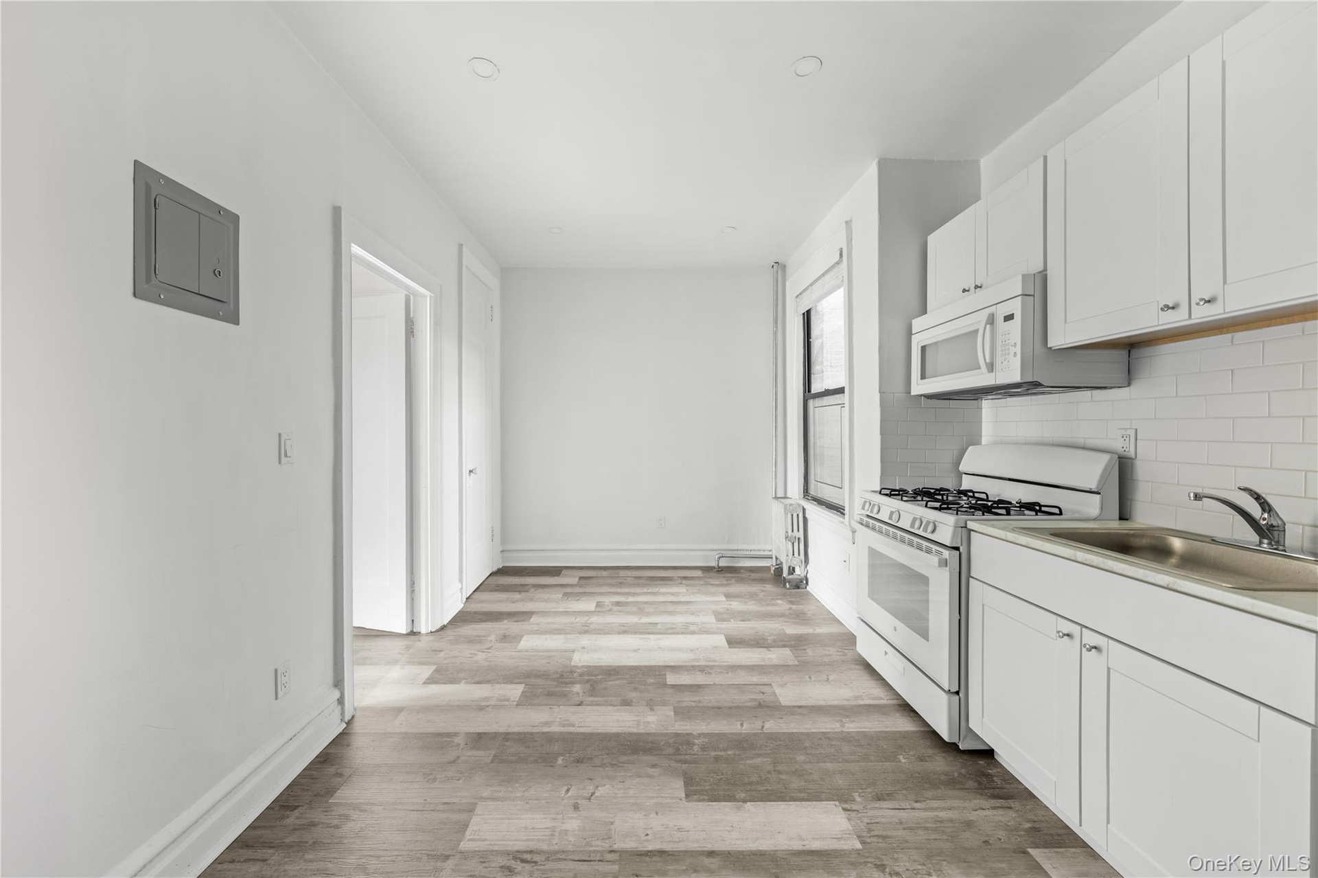 Kitchen with white appliances, electric panel, tasteful backsplash, light wood-type flooring, and white cabinets