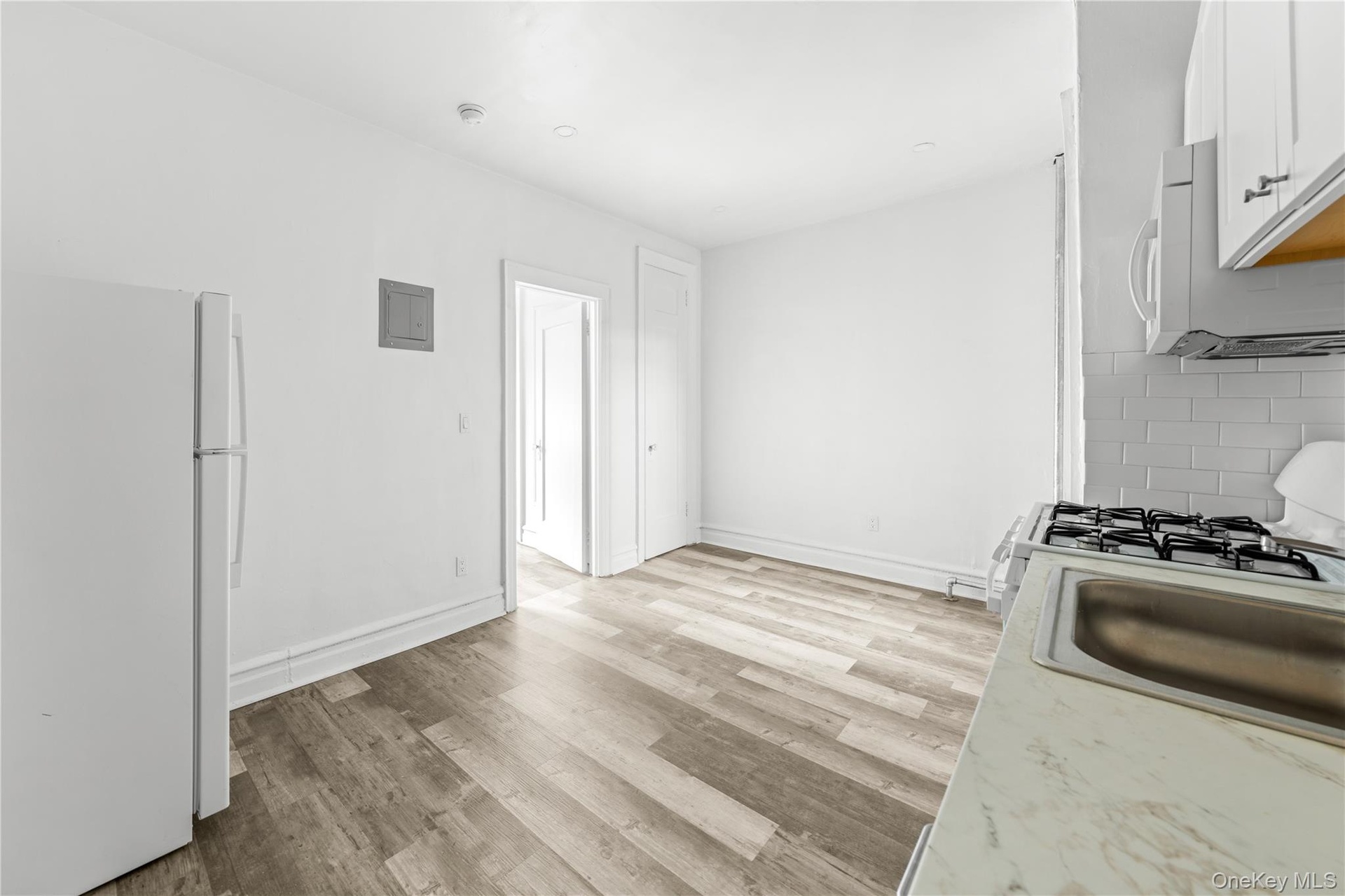Kitchen with white appliances, light wood-style flooring, light countertops, white cabinets, and backsplash