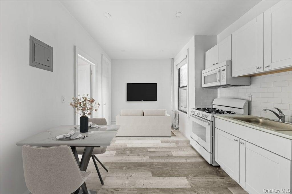 Kitchen featuring white appliances, light wood-style flooring, decorative backsplash, and white cabinetry