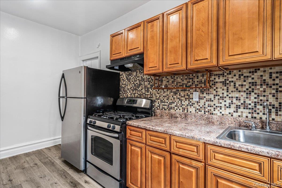 Kitchen with stainless steel gas stove, wood finished floors, under cabinet range hood, and brown cabinetry