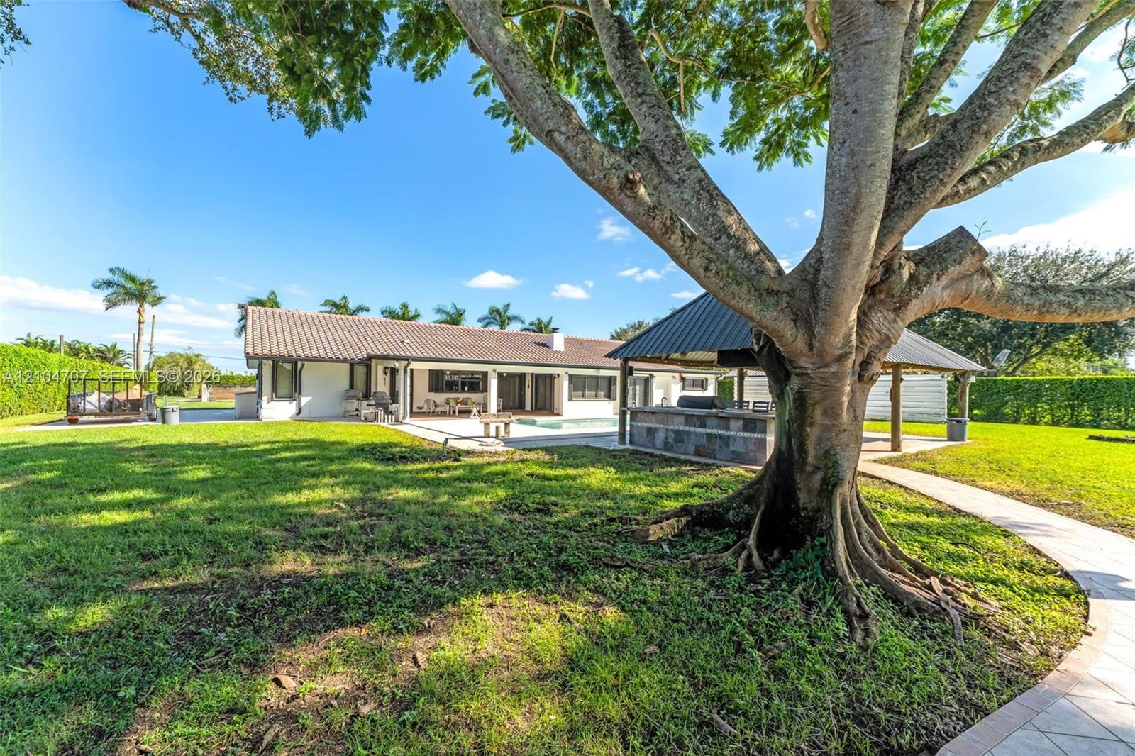 Expansive pasture featuring metal perimeter fencing, a covered storage structure with a metal roof, and established perimeter hedging