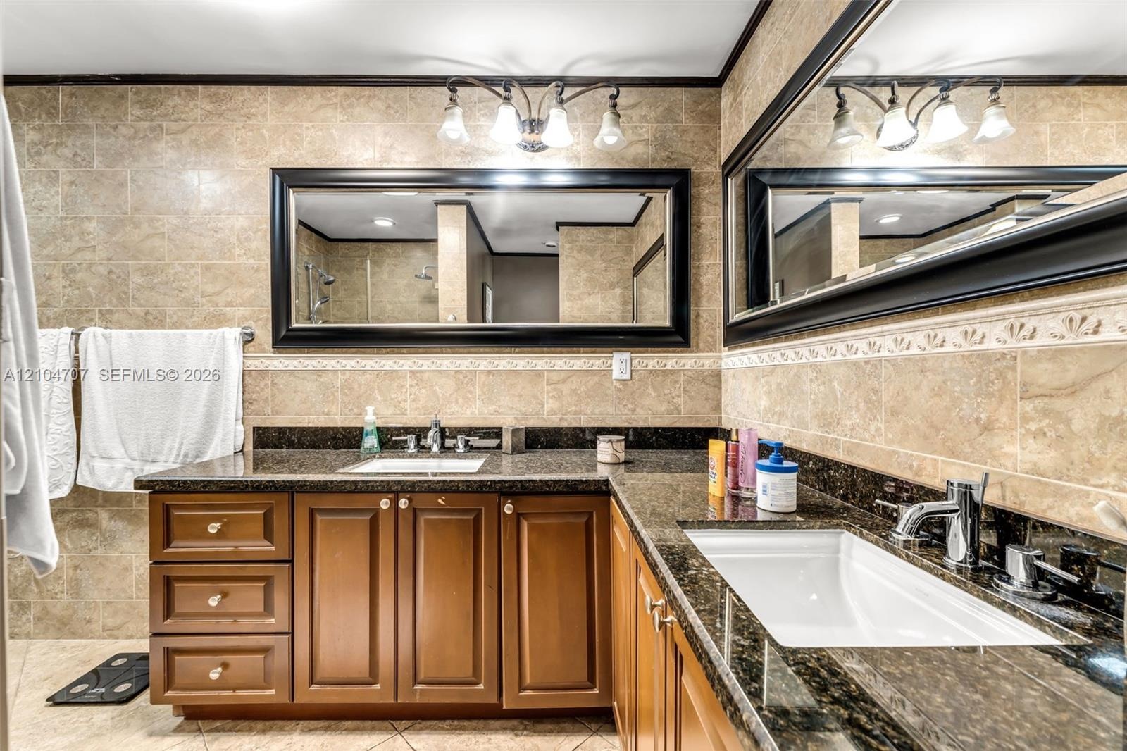 Bathroom featuring floor-to-ceiling stone-finish tile, glass-enclosed shower with a multi-function showerhead, dark stone-finish vanity countertop, an